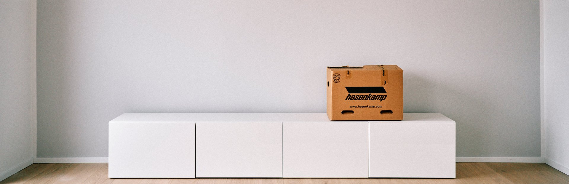 Ein leerer Raum mit einem Sideboard, auf dem eine Umzugskiste mit hasenkamp Aufdruck steht.