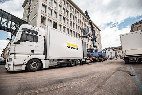 Ein Kran lädt eine schwere Last auf einer Palette in einen hasenkamp LKW.